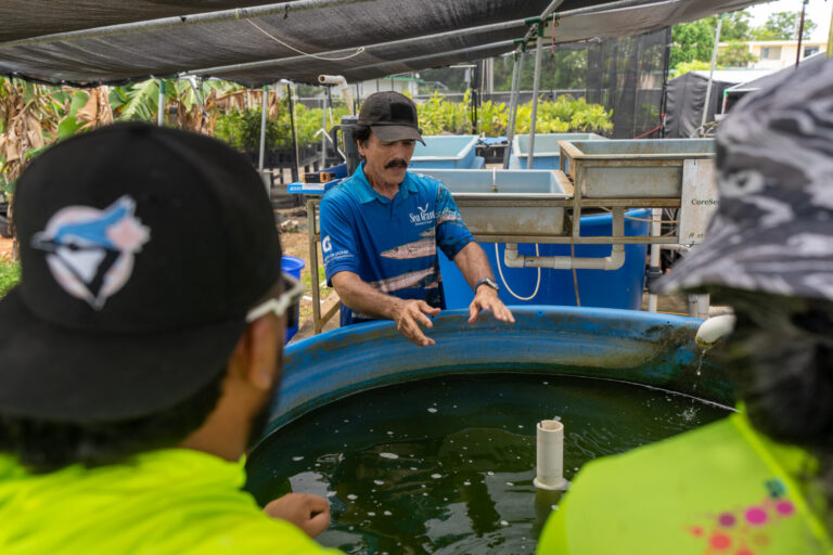Dave Crisostomo wearing a blue polo shirt standing with an aquaponics system with live fish inside.