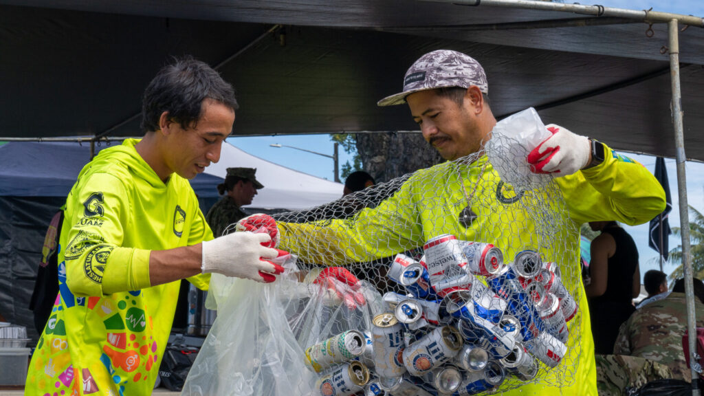 Gideon Tyquienco and Matthew Pangelinan transfer aluminum from a can bin into a trash bag.