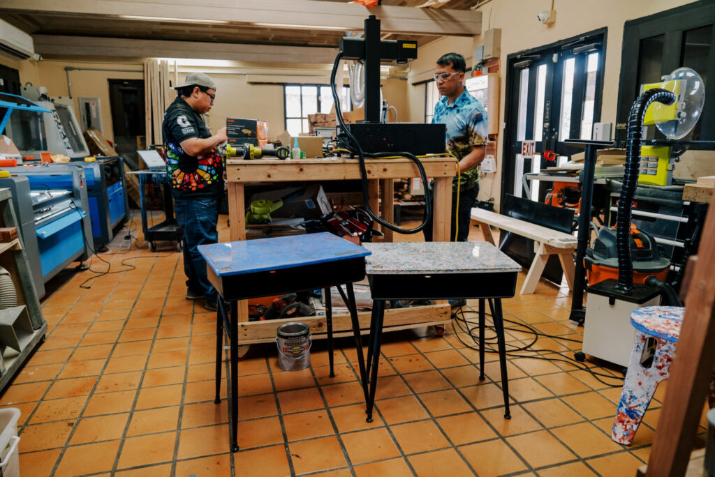 The G3 Makerspace & Innovation Hub team operates the machines that produce desktops from recyclable plastics #2 and #5. The photo also showcases two desk prototypes created by the G3 Makerspace for their desk refurbishment project.