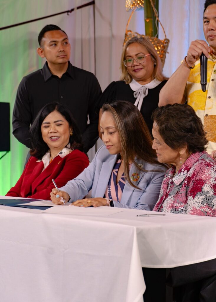 GVB President Regine Biscoe Lee signs an MOU as UOG President Anita Borja Enriquez (left) and Governor Lourdes Leon Guerrero (right) observe.