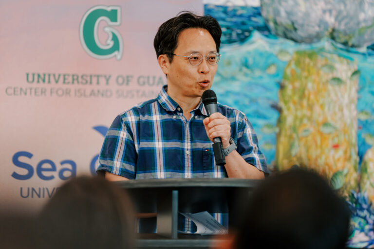 Dr. Yong Sang Kim speaks into a microphone at a podium during the UOG Sea Grant research funding announcement.