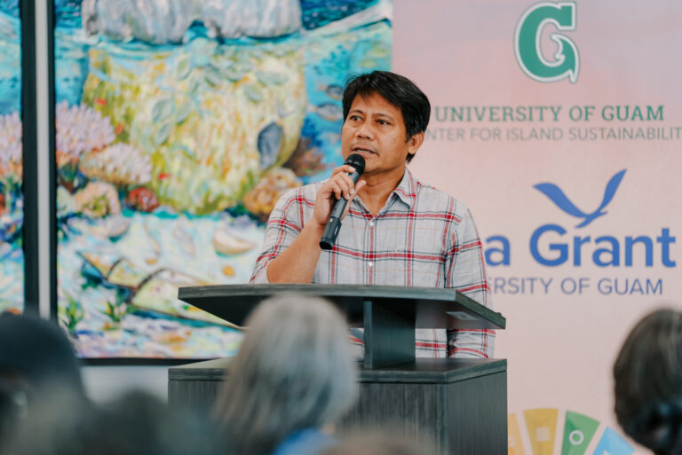 Dr. Ernesto Guades speaks into a microphone at a podium during the UOG Sea Grant research funding announcement.