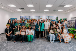 A group graduation photo of the G3 Conservation Corps and Youth Conservation Corps, posing indoors with certificates, flower crowns, and UOG leaders.