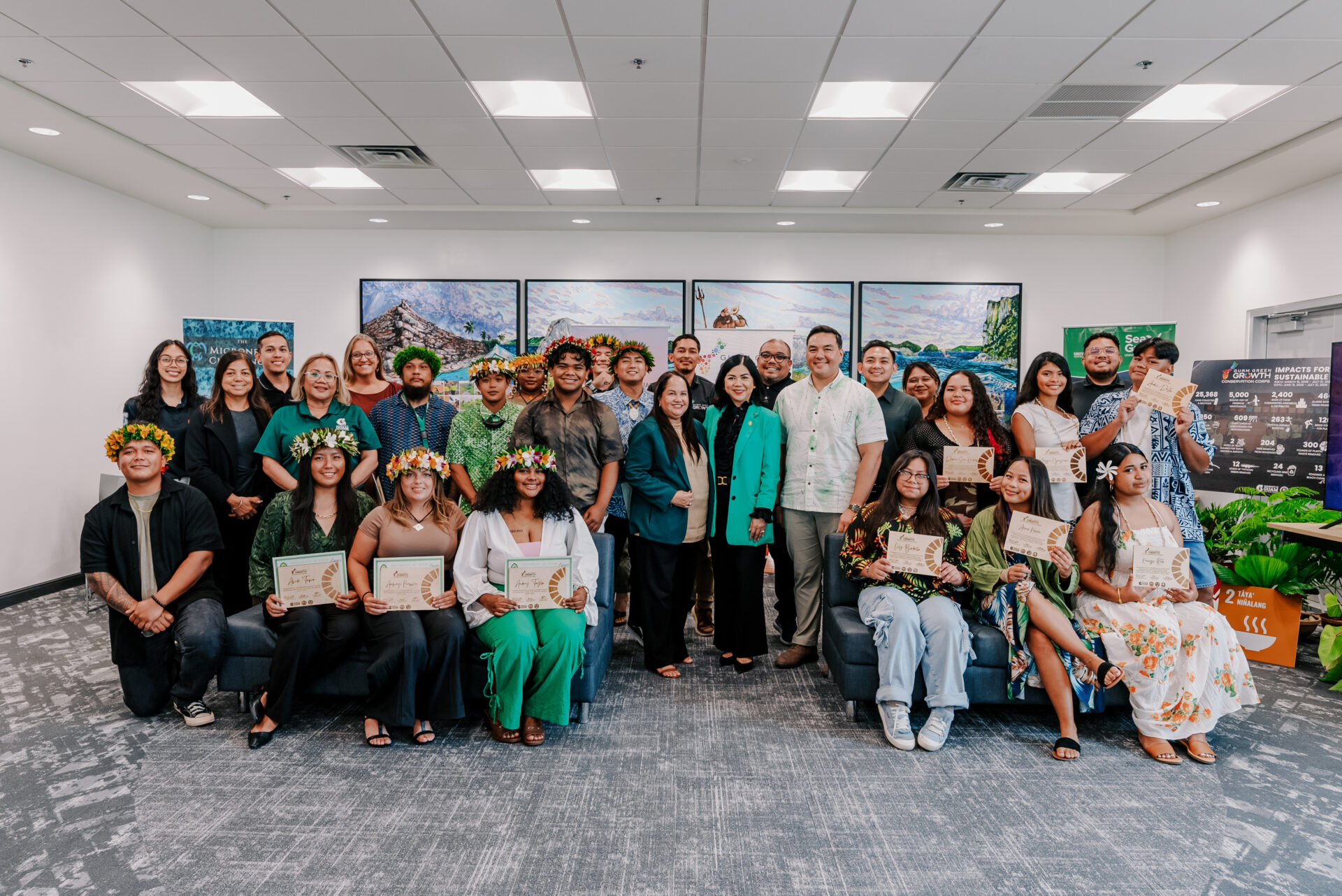 A group graduation photo of the G3 Conservation Corps and Youth Conservation Corps, posing indoors with certificates, flower crowns, and UOG leaders.