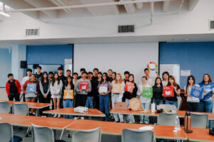 Junior Achievement Guam high school students pose with G3 Makerspace Coordinator Abby Crain while holding colorful UN Sustainable Development Goal posters.